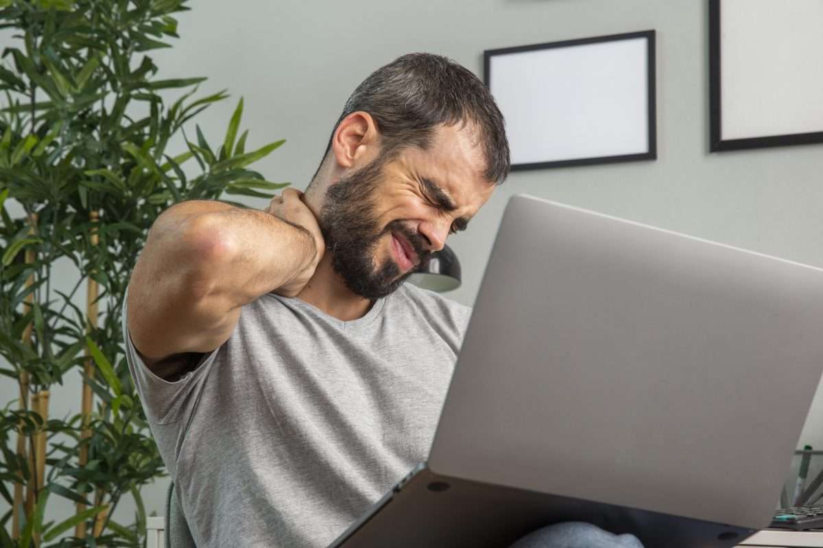 Man experiencing neck pain while working on a laptop with bad posture.